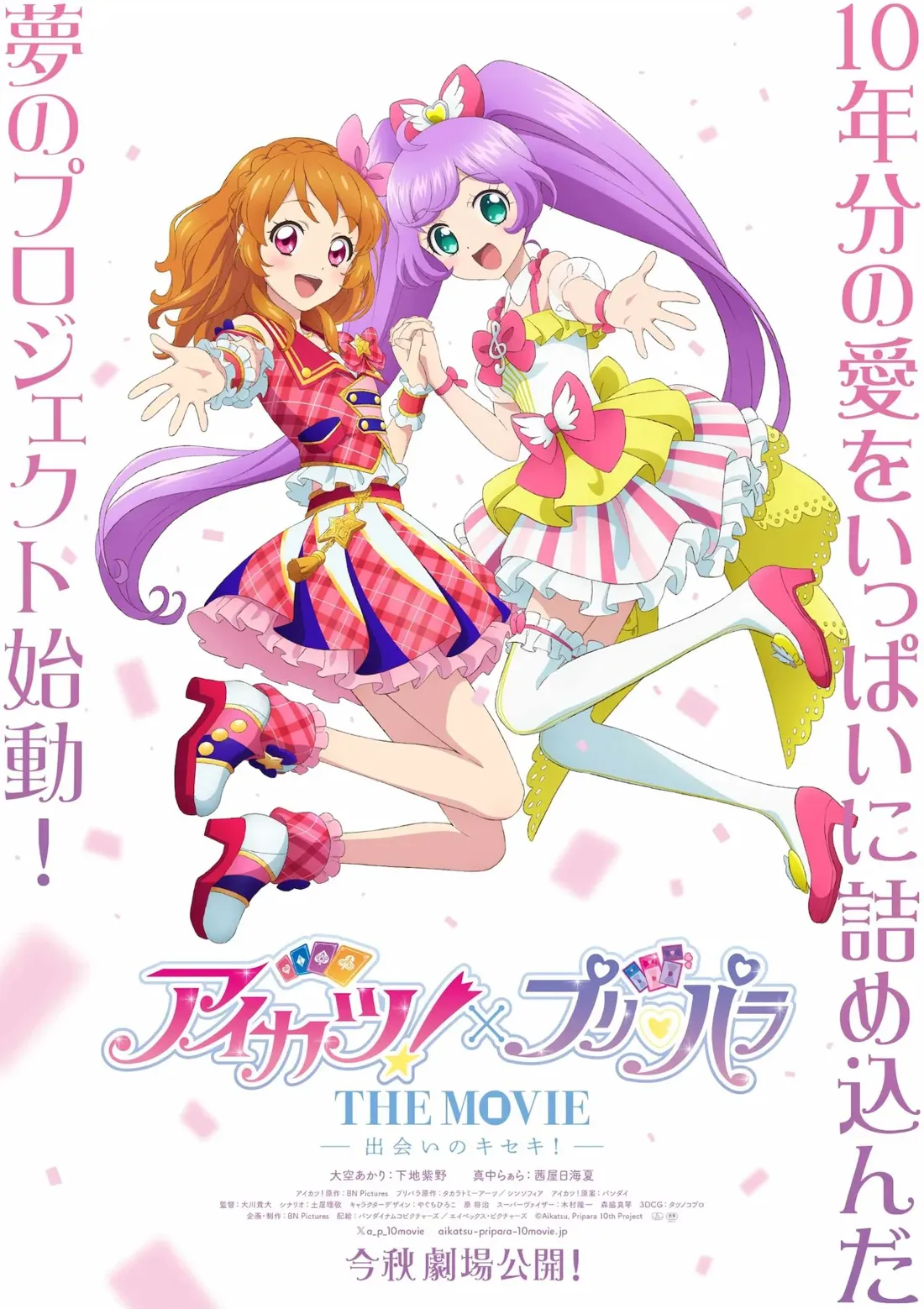 Promotional poster for the anime movie *Aikatsu! x Pripara: The Movie - The Miracle of Meeting!* The poster features two female anime characters, holding hands, against a pink and white background with confetti. The character on the left has bright orange hair styled in pigtails, wearing a red, pink, and white plaid dress with a gold star accent, and dark pink shoes with yellow accents. The character on the right has long purple hair styled in high ponytails and wears a light pink and yellow dress with pink and white stripes and white thigh-high socks. Both girls are in mid-air, dynamically posed, radiating a cheerful energy. The movie title, 'アイカツ!×プリパラ THE MOVIE,' is prominently displayed at the bottom, along with Japanese text that translates to English promotional information including the release date. The artistic style is typical of bright, colorful anime promotional materials, characteristic of the *Aikatsu!* and *Pripara* franchises.